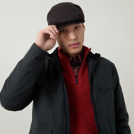 Model with Barbour Barlow Logo Patch Flat Cap in brown herringbone tweed, styled with dark jacket and red knitwear