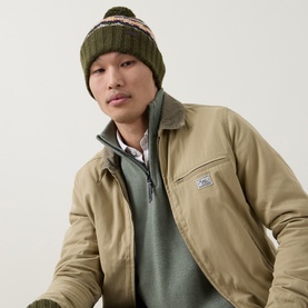 Model wearing Barbour Kane Beanie Hat in Dark Green with Fair Isle knit and bobble pom, styled with a beige jacket and green jumper.