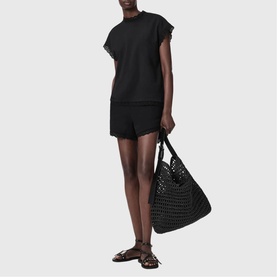 Model wearing All Saints Lele Lace Trim Top in black with matching black shorts, carrying a woven black tote bag, styled with brown flat sandals.