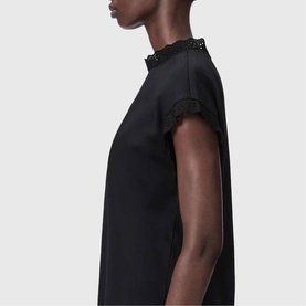 Model wearing All Saints Lele Lace Trim Top in black with lace-trimmed mock neck and short sleeves with lace trim detail.
