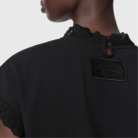 Model wearing All Saints Lele Lace Trim Top in black, close-up of back detail showing lace trim, button-loop closure and embroidered logo patch.
