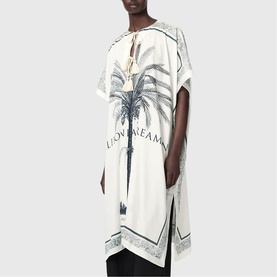 Model wearing All Saints Tess Printed Logo Kaftan in ecru white with palm tree print, tassel ties, and side slits.
