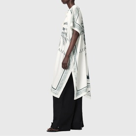 Model wearing All Saints Tess Printed Logo Kaftan in ecru with dark graphic print, styled with wide-leg black trousers and sandals.