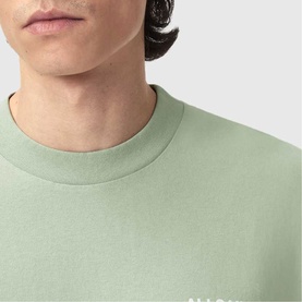 Model wearing sage green crew neck T-shirt with small white logo print at chest, close-up detail view