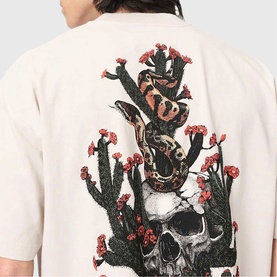 Model wearing All Saints Cacti Oversized Graphic T-Shirt in Dusk White, showing back with snake, skull and cactus screen print.