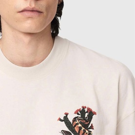 Model wearing All Saints Cacti Oversized Graphic Logo T-Shirt in Dusk White with snake and cactus screen-print detail on chest.