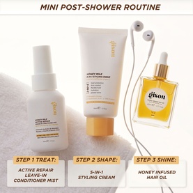 Gisou Honey Milk mini post-shower haircare routine set with Leave-In Conditioner Mist, Styling Cream, and Honey Infused Hair Oil on a white towel.