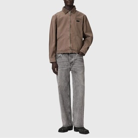 Model wearing All Saints Korey Canvas Jacket in Mire Brown with zip closure and chest pocket, styled with grey wide-leg jeans.