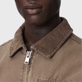 Model wearing All Saints Korey Canvas Jacket in Mire Brown, close-up showing zip closure and corduroy collar detail.