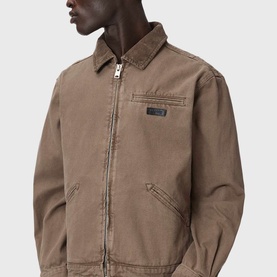Model wearing All Saints mire brown zip-up jacket with collar, chest pocket detail and small logo badge.
