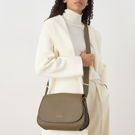 Model carrying MMK Holmes Logo Crossbody Bag in Loden leather, gold-tone hardware, flap closure, worn on shoulder with adjustable strap.