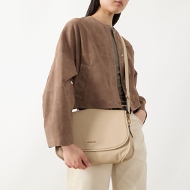 Model carrying MMK Holmes Logo Crossbody Bag in khaki grained leather with gold-tone hardware, worn as crossbody, styled with camel jacket and
