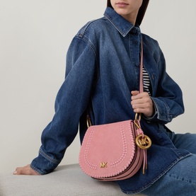 Model carrying MMK Josie Saddle Crossbody Bag in Primrose pink leather with gold-tone hardware, branded keychain, and tonal braided trim
