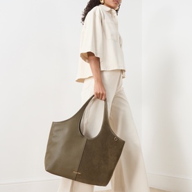 Model carrying MMK Henley Shopper Tote Bag in Loden suede, gold-tone hardware, shoulder straps, styled with cream oversized top and wide-leg trousers