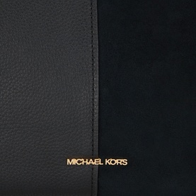 Michael Kors black leather tote bag close-up showing contrast suede panel and gold logo lettering