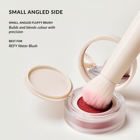 Duo Brush 2.0 small angled fluffy brush resting on open compact of deep red powder blush, showing precision application tip