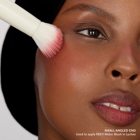 Model with Duo Brush 2.0 applying blush to cheek, white handle brush with pink and white bristles shown in use