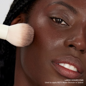 Model applying Duo Brush 2.0 to cheek, large domed end shown, used with REFY Water Bronzer in Selene