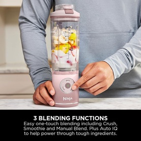 Ninja Blast Max Cordless Portable Blender in pink, shown in use blending fruit chunks, with one hand steadying the cup on base.