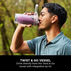 Model drinking from Ninja Blast Max Cordless Portable Blender in pink, using integrated sip lid, outdoors in natural setting