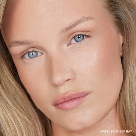 Model wearing No Brand UDA Water Bronzer in shade Bay, shown as a close-up face shot with a natural, sun-kissed glow.