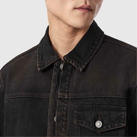 Model wearing All Saints Roth Denim Jacket in overdyed brown, close-up showing collar, silver button fastenings and chest pocket detail.