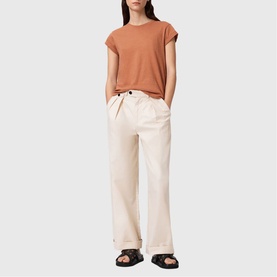 Model wearing All Saints Anna Back Logo T-Shirt in Pecan Brown with cream wide-leg trousers and black sandals.