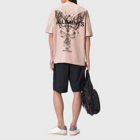 Model wearing All Saints Hallis Oversized Graphic Logo T-Shirt in Sunbaked Pink with black back graphic, styled with black shorts.