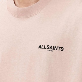 Model wearing AllSaints crew neck t-shirt in Sunbaked Pink with small logo print to chest