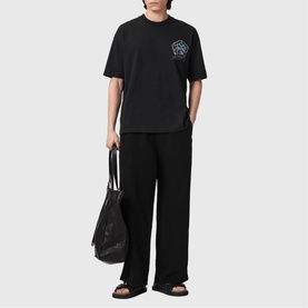 Model wearing black graphic T-shirt and wide-leg trousers, carrying a black tote bag