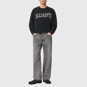 Model wearing All Saints Dash Logo Sweatshirt in Washed Black with crew neck and logo print, styled with grey wide-leg jeans