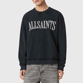 Model wearing AllSaints Dash Logo Sweatshirt in Washed Black with crew neck, distressed logo graphic, styled with grey jeans.