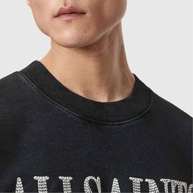 Model wearing All Saints Dash Logo Sweatshirt in Washed Black, crew neck with distressed logo graphic, close-up shot.