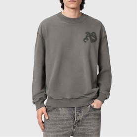 Model wearing All Saints Insignia Logo Sweatshirt in Washed Black with gothic snake appliqu&eacute;, crew neck, styled with grey jeans.