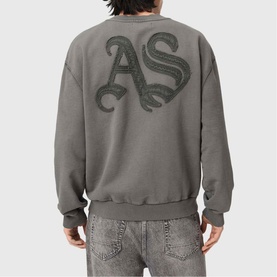 Model wearing All Saints Insignia Logo Sweatshirt in Washed Black, back view showing gothic AS appliqu&eacute; logo, styled with grey jeans.