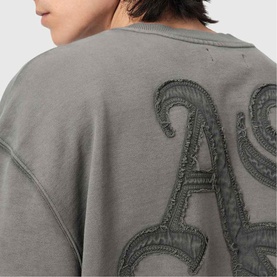 Model wearing All Saints Insignia Logo Sweatshirt in Washed Black, showing back detail with gothic appliqu&eacute;d logo embroidery and distressed finish.