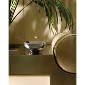 Alessi Diffuser Set in polished stainless steel canister with spoon rest, styled on a gold surface beside tropical foliage