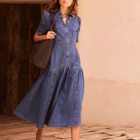 Model wearing Mint Velvet blue denim midi dress with zip front, short sleeves, and tiered skirt, styled with a brown woven shoulder bag