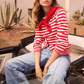 Model wearing Mint Velvet red and white striped top, tied at waist, styled with a red scarf and light blue wide-leg jeans