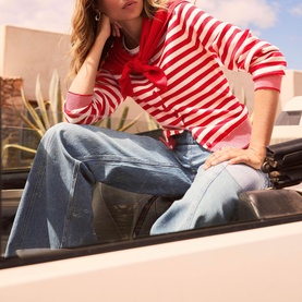 Model wearing Mint Velvet red and white stripe top with red bow detail, styled with light wash wide-leg jeans