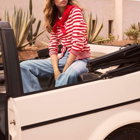 Model wearing Mint Velvet red and white striped top with wide-leg blue jeans, seated on a white convertible car outdoors.