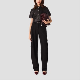 Model wearing Maje red French dress styled with black cargo trousers, leather belt, and carrying a dark burgundy clutch bag, with dark heels.