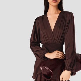 Model wearing deep brown satin wrap blouse with V-neckline, elasticated waist and flared cuffs, styled with burgundy velvet skirt and clutch