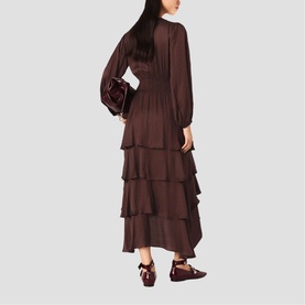 Model wearing dark brown long-sleeve tiered maxi dress with smocked waist, styled with a burgundy bag and mary jane heels