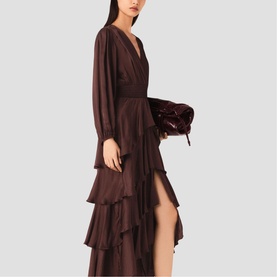 Model wearing chocolate brown long-sleeve V-neck tiered ruffle maxi dress with thigh-high split, carrying dark burgundy velvet clutch bag