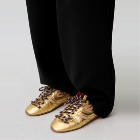 Model wearing Claude Pierlot metallic gold leather trainers with leopard-print laces, styled with black wide-leg trousers