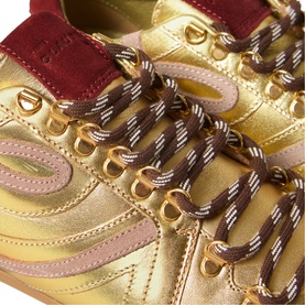 Claude Pierlot metallic gold trainers with burgundy suede heel panel, striped laces, and gold-tone eyelets, close-up detail view