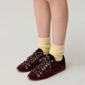Model wearing Claude Pierlot red suede lace-up trainers with tan sole, styled with yellow ribbed ankle socks