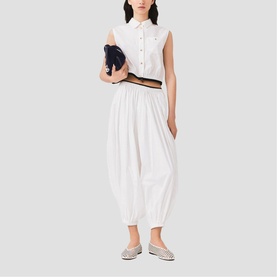 Model wearing white sleeveless cropped shirt and white balloon-leg trousers, carrying a navy clutch, styled with silver metallic flat shoes