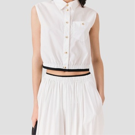 Model wearing Maje white sleeveless cropped shirt with gold buttons and chest pocket, styled with wide-leg white trousers and black waistband detail.